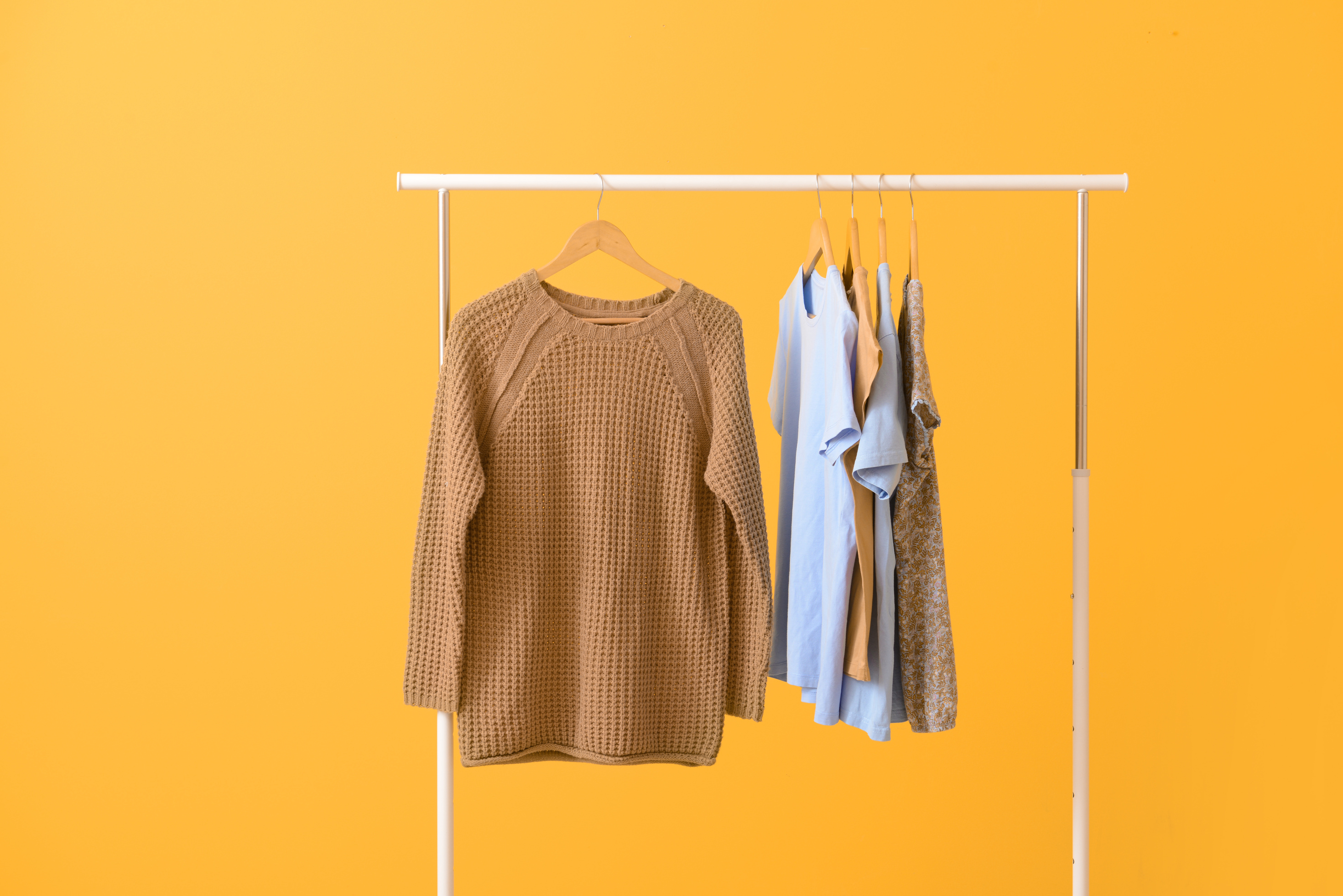 Rack with Hanging Clothes on Color Background
